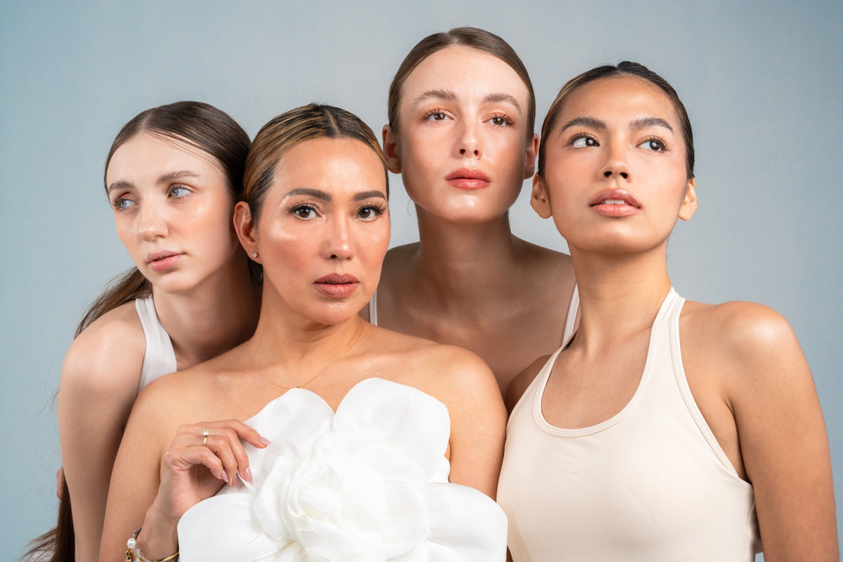 Four women in white outfits posed together against a soft blue backdrop